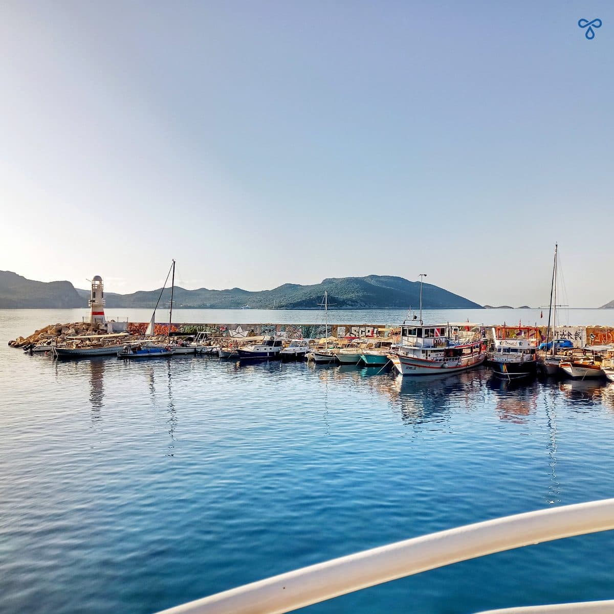 Kaş harbour wall with a small lighthouse to the left. The rails of the ferry are in the foreground.