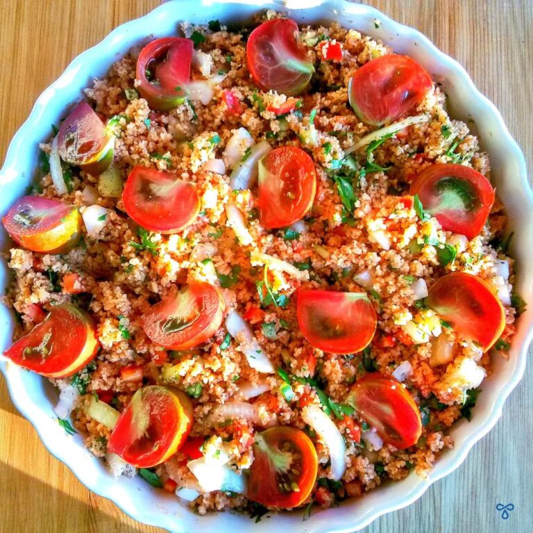 A circular bowl photographed from above. The bowl contains bulgur wheat, wedges of cherry tomatoes and sliced onions.