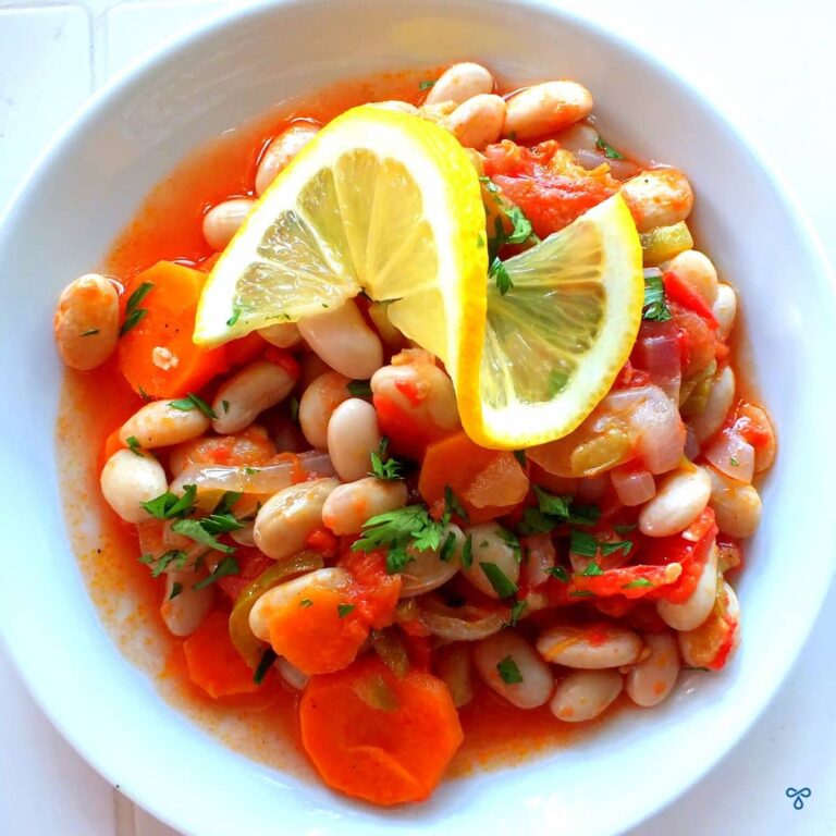 Borlotti beans cooked with onion and carrot in olive oil and tomatoes. The beans are topped with a curled slice of lemon