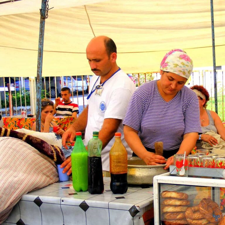 A woman and man behind a counter making kar şerbeti. The woman is pounding ice with a pestle and mortar.