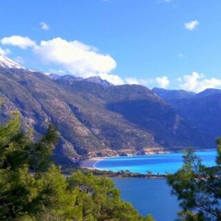 A view of the Ölğdeniz lagoon from above. Pine tree tops frame the view and snow-capped mountains back onto the turquoise water