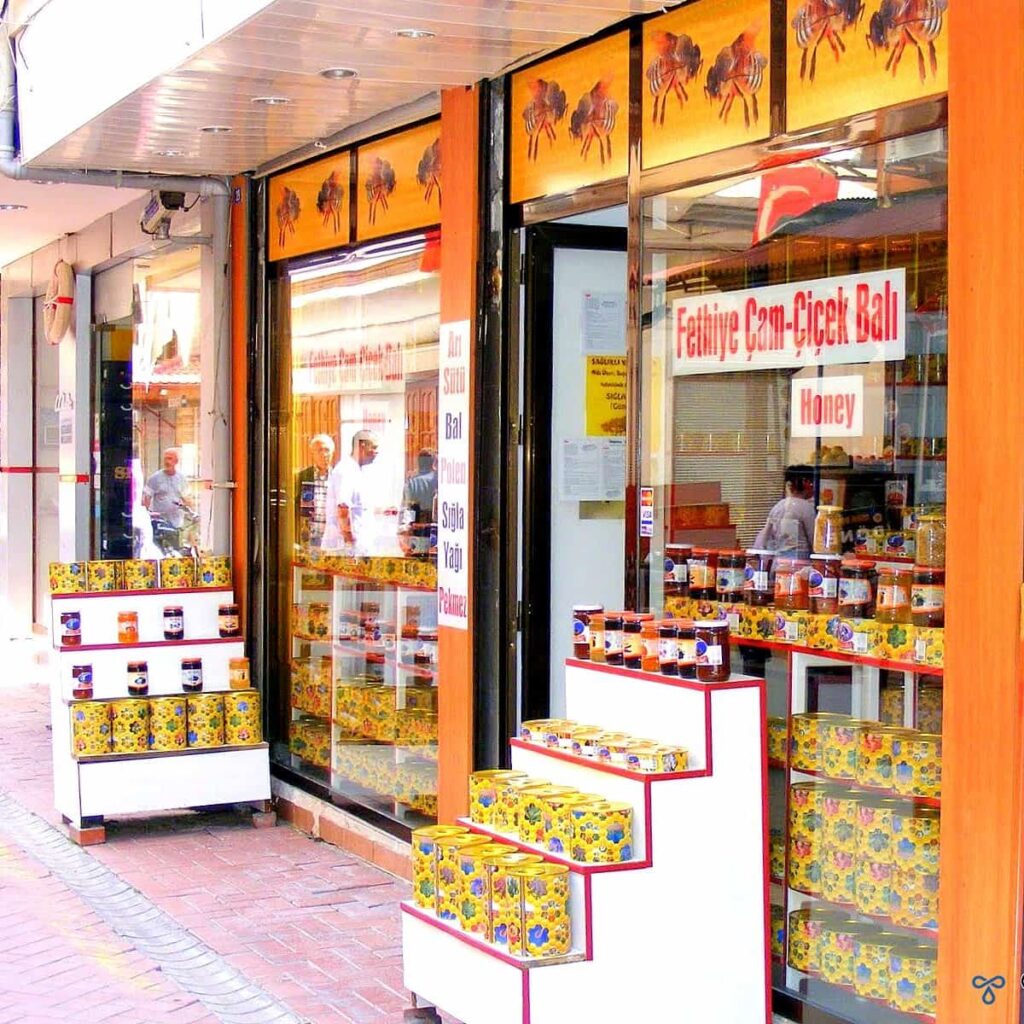 Frontage of a honey shop in Fethiye. A yellow banner over the top has photos of honey bees and there are display stands outside with tins of honey and jars of jam and molasses.