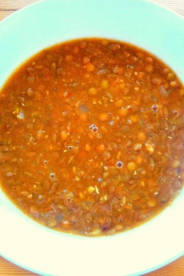 A bowl of soup viewed from above. Green lentils are visible in the brown broth.