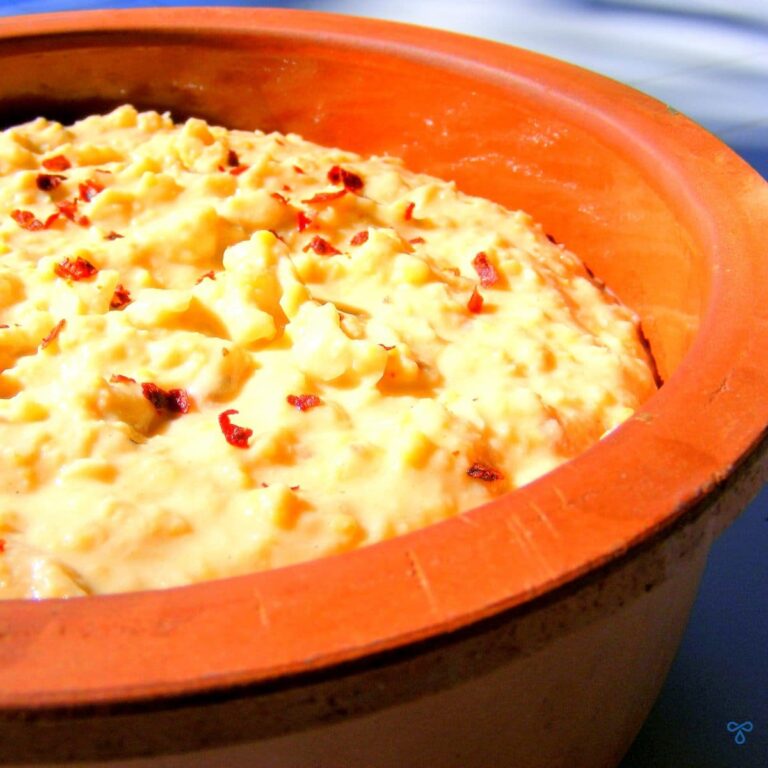 A terracotta bowl filled with hummus and topped with a sprinkling of chill flakes