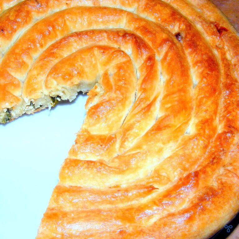 A big spiral phyllo pastry pie with a slice cut out of it.