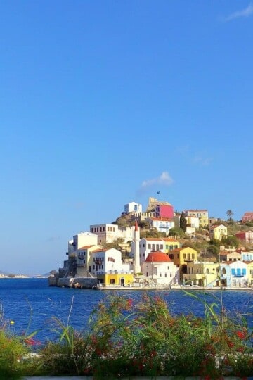 A view across the harbour of Kastellorizo. Colourful buildings, including a mosque and a castle, climb up the hillside.
