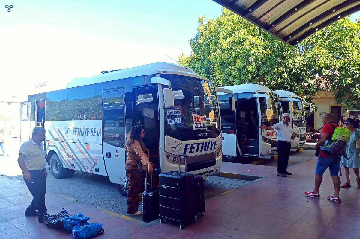 Three midibuses at their platform in Fethiye Otogar. Some people are waiting with luggage.