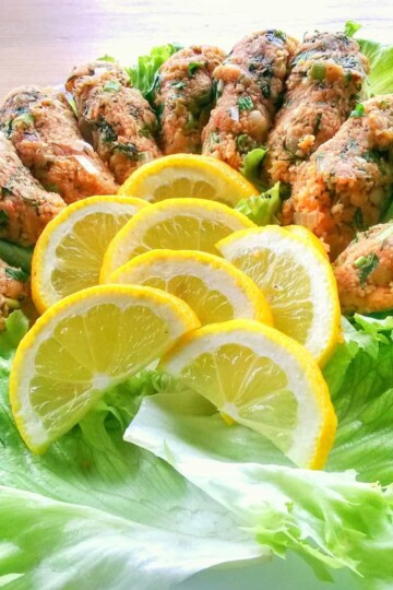 Pieces of lentil köfte laid on top of lettuce leaves. Slices of lemon are arranged in the centre.