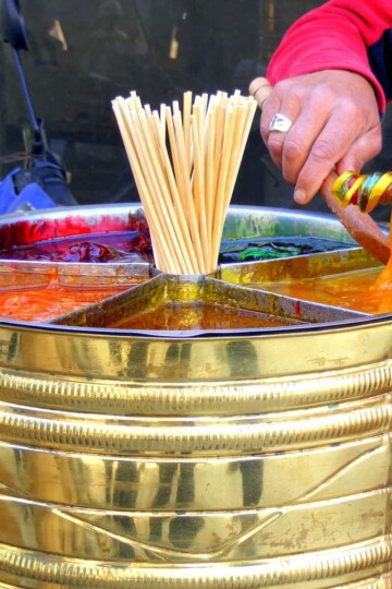 a brass barrel with multicolıured soft sweets in it. A vendor is twisting the colours around a stick.