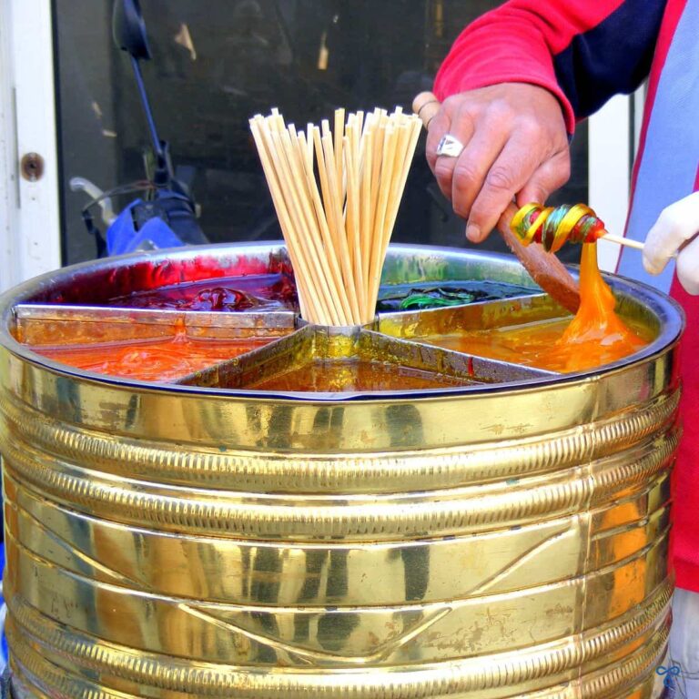 a brass barrel with multicolıured soft sweets in it. A vendor is twisting the colours around a stick.