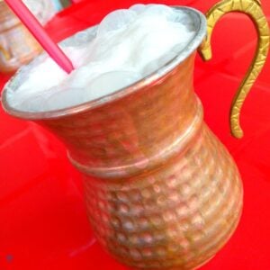 A copper cup with frothy ayran yoghurt drink bubbling over the top.