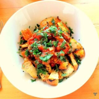 A white bowl filled with fried bread croutons and topped with sauteed beef in tomato sauce. Fresh chopped parsley leaves garnish the dish.
