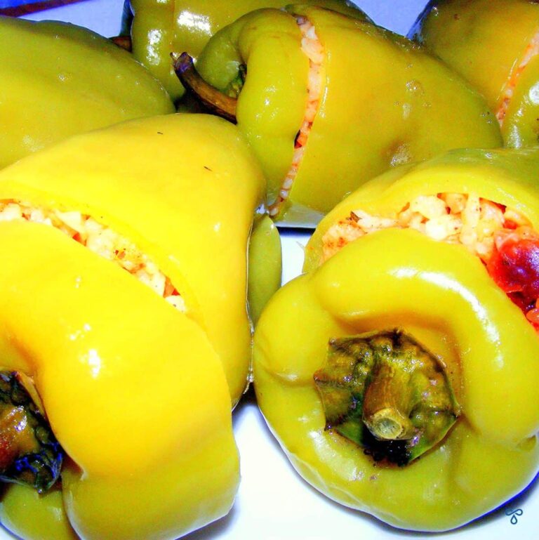 Cooked green bell peppers lying on their side and stuffed with rice. The lids are on the peppers
