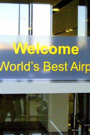 A sign on a glass door reads Welcome to World's Best Airport. The sign is written in yellow lettering.