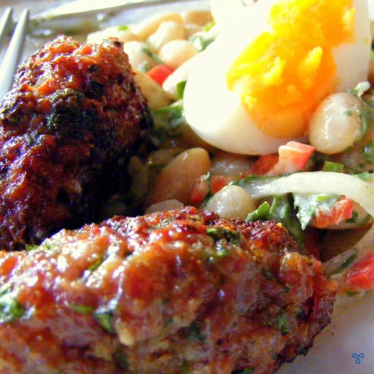 Two oblong meatballs with bean salad and a slice of hard boiled egg.