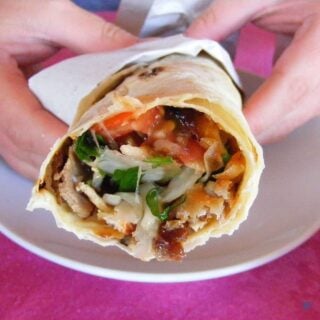 A Turkish lavaş wrap with the filling visible inside. Strips of meat and salad are visible.