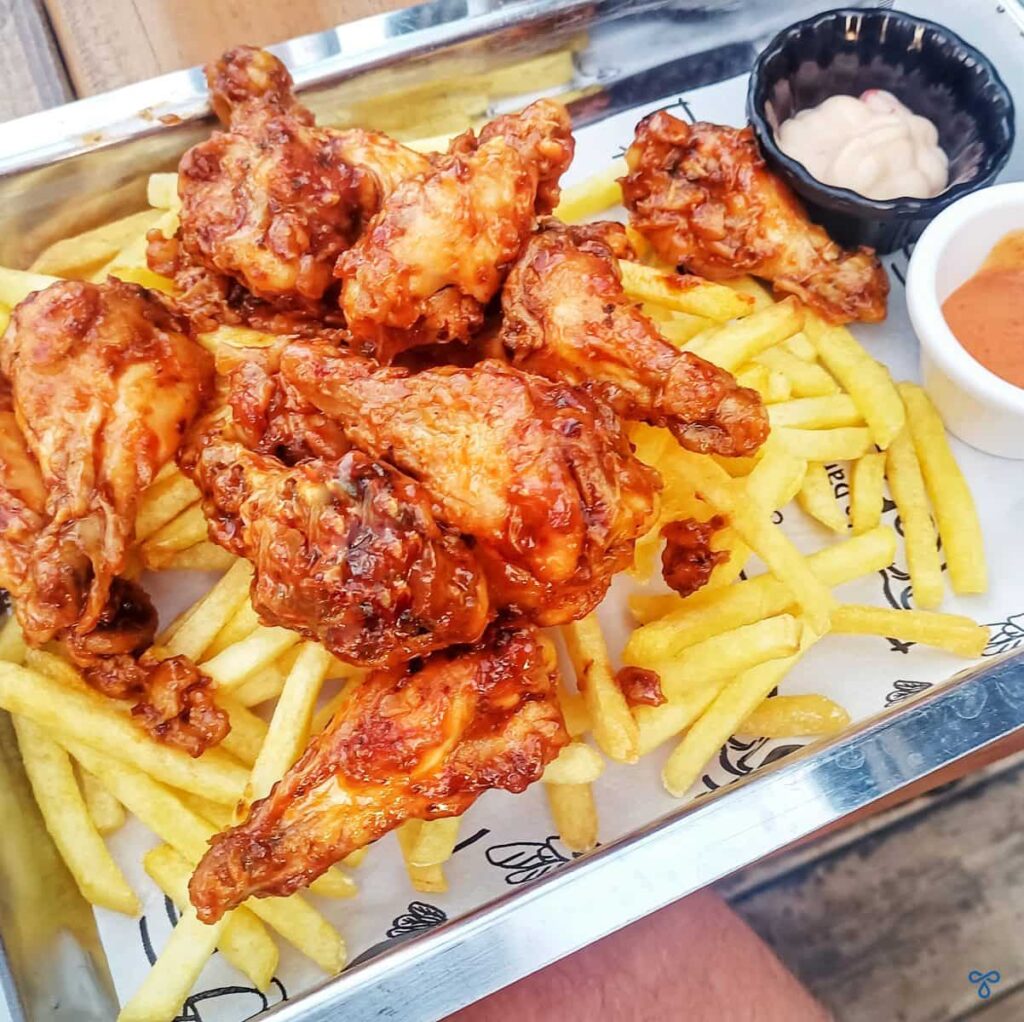 Buffalo chicken wings served on top of fries. Two ramekins with dips are on the side.