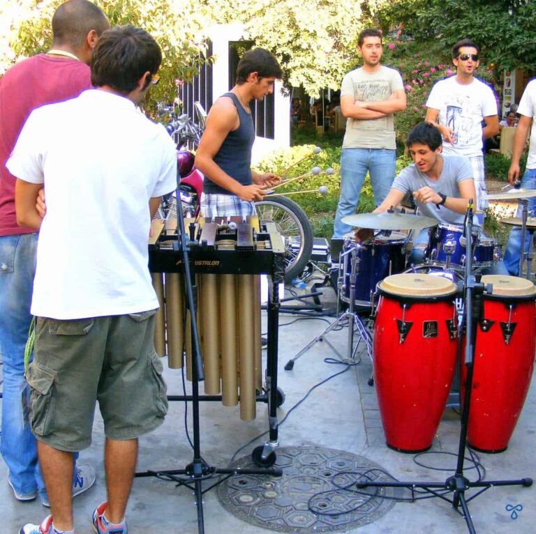 Street musicians setting up drums and xylophone under the watch of onlookers