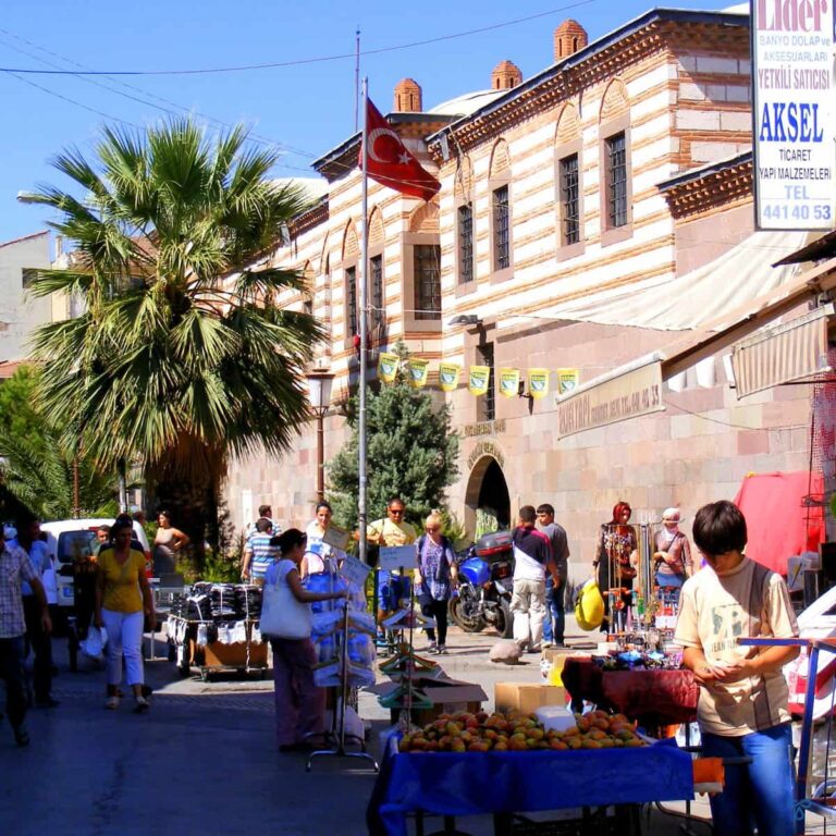 A city scene in a historic area. A young street trader is selling fruit from a cart in the foreground.