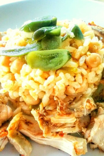 A cylindrical pile of cooked rice and chickpeas surrounded by chicken pieces and topped with jalapenos.