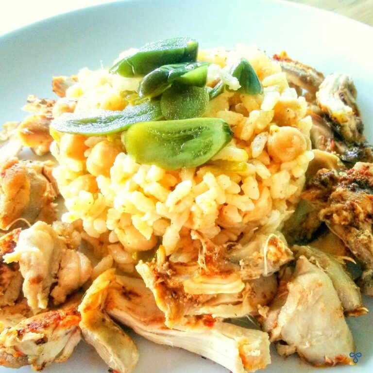 A cylindrical pile of cooked rice and chickpeas surrounded by chicken pieces and topped with jalapenos.