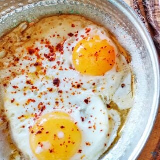 Two fried eggs in a pan. Both topped with red pepper flakes