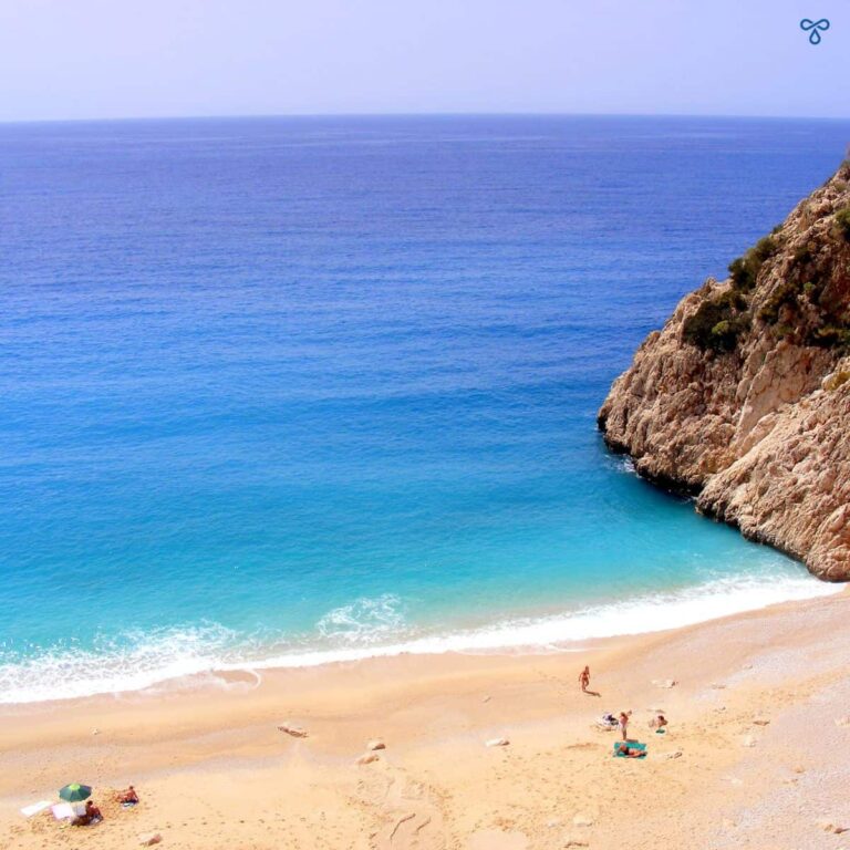 A view of a deserted sandy beach from. A cliff face is to the left and then open sea ahead.