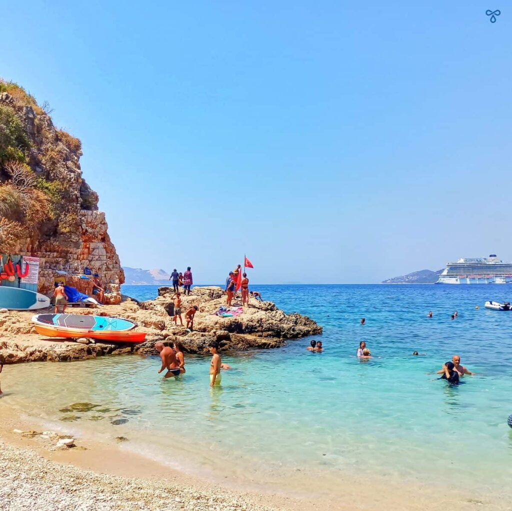 Swimmers on a rock at Big Pebble Beach in Kaş. People are swimming and the clear sea is lapping the beach.