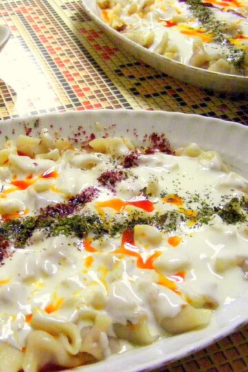 A section of a plate of mantı - small dumplings covered in yoghurt and oil and crisscrossed with dried mint sprinkles.