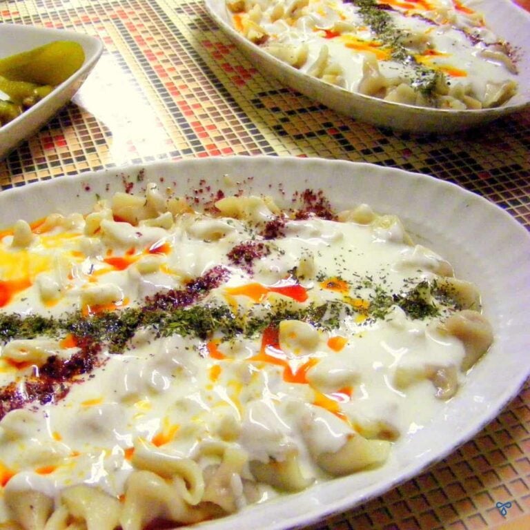 A section of a plate of mantı - small dumplings covered in yoghurt and oil and crisscrossed with dried mint sprinkles.