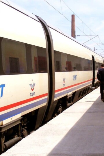 Two carriages of a white high speed train in a station. Passengers walk along the platform to the right of the train.