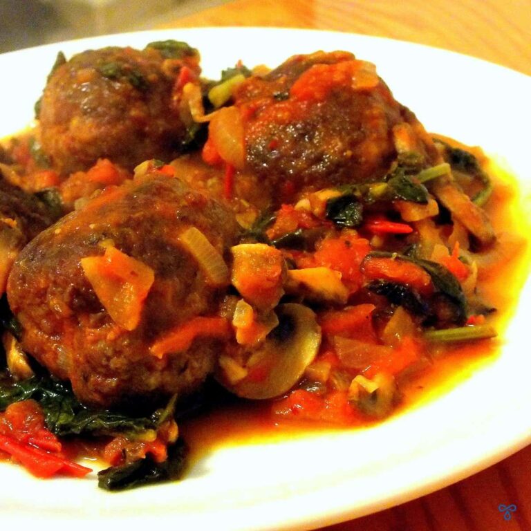 Three rounded meatballs in a tomato and vegetable sauce