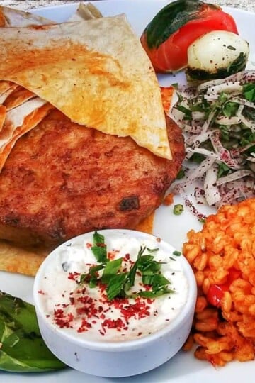 Şato piliç, a chicken burger served with bulgur wheat, onion and grilled tomato. flatbreads are on the side.