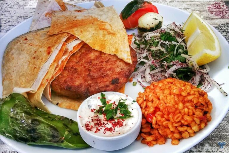 Şato piliç, a chicken burger served with bulgur wheat, onion and grilled tomato. flatbreads are on the side.