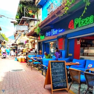 A street view outside Deep Blue Bar in Fethiye. A board advertises drink prices and a neon sign advertises pizza.
