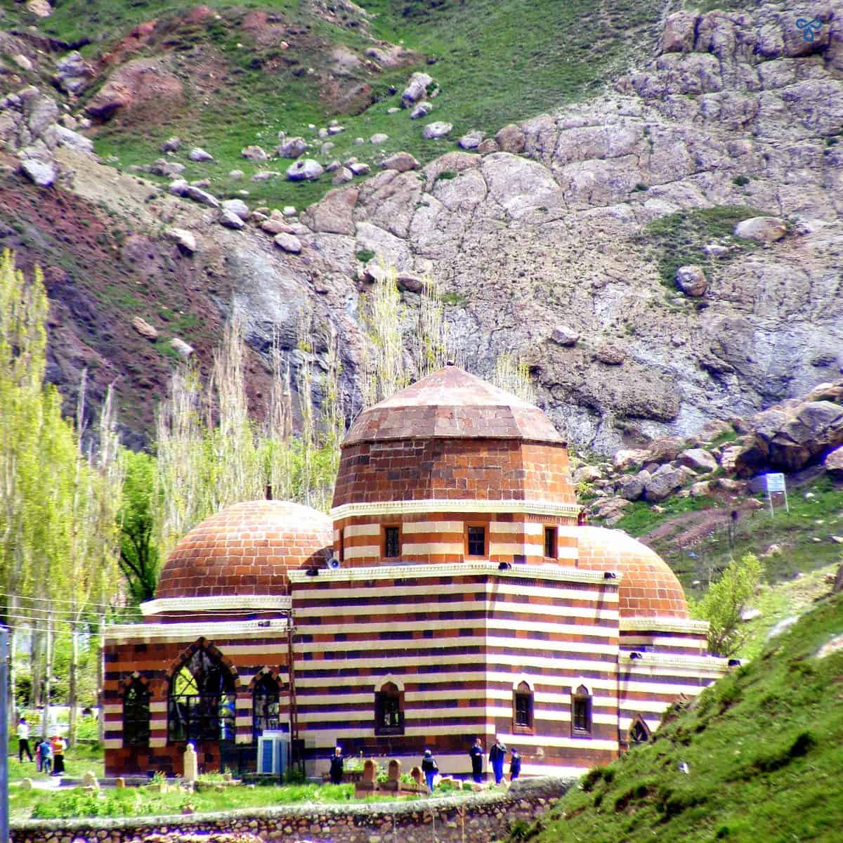 The striped Grand Tomb in Doğubeyazıt, East Turkey. The tomb is on a mountain plateau with trees behind it.