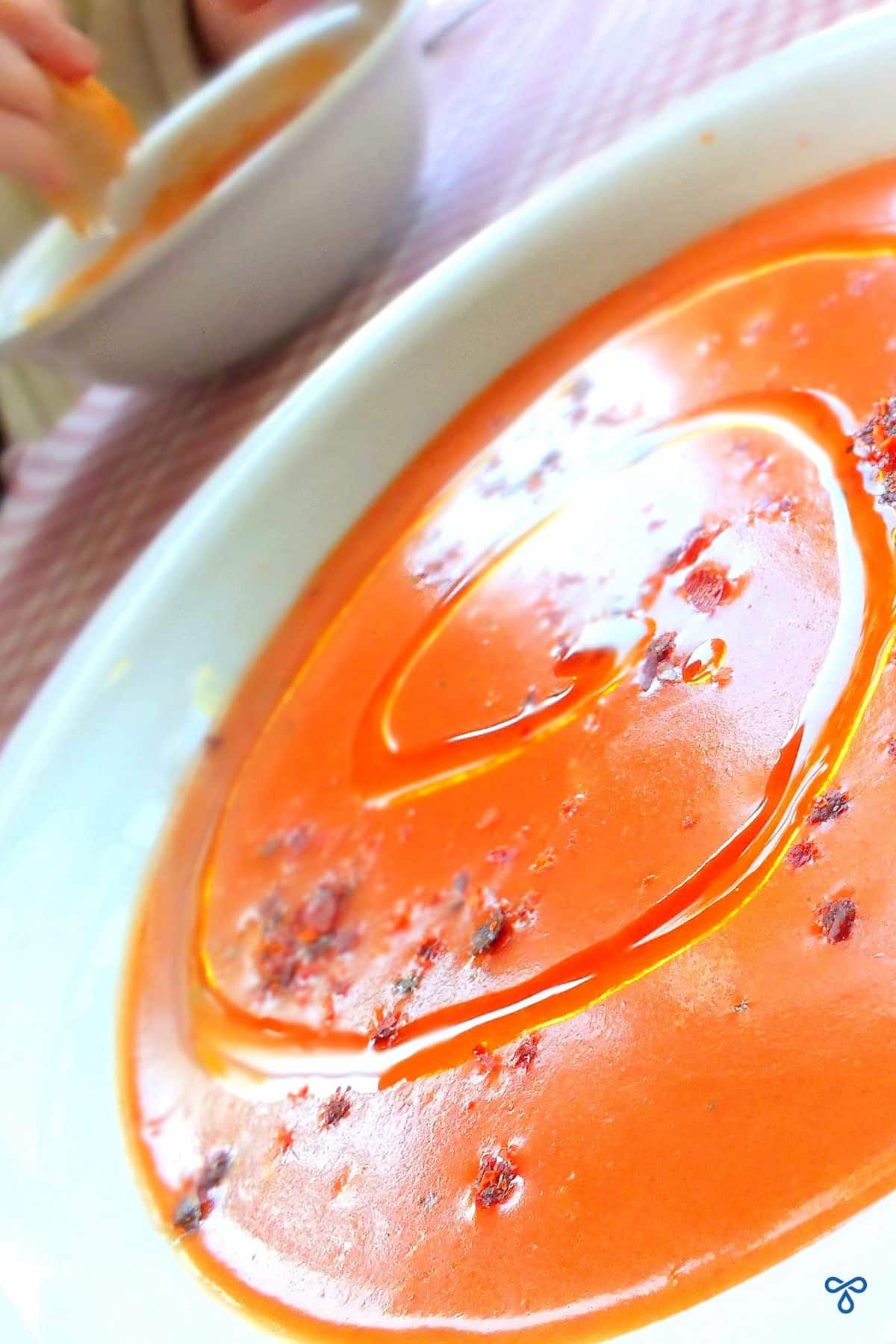 A portrait image of tangy rust-coloured tarhana soup. It is drizzled with oil and topped with chilli flakes.