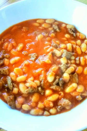 A bowl of Turkish kuru fasulye - haricot beans in a tomato sauce. There are also small chunks of lamb in the sauce.