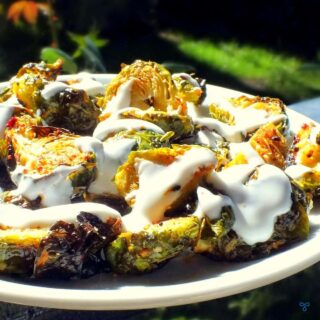 Roasted Brussels Sprouts sliced in half and drizzled with yoghurt. On a white plate.