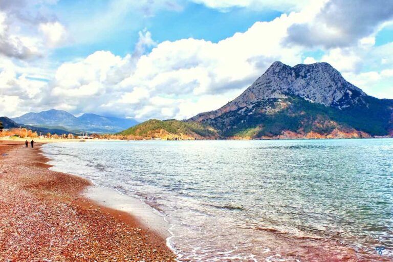 Adrasan Bay - calm sea lapping on a sand and shingle beach. A rocky hill is in the background.