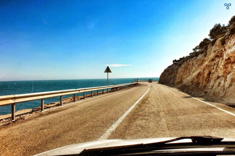 The road ahead viewed through a car windscreen. Sea is to the left and a cliff face to the right.