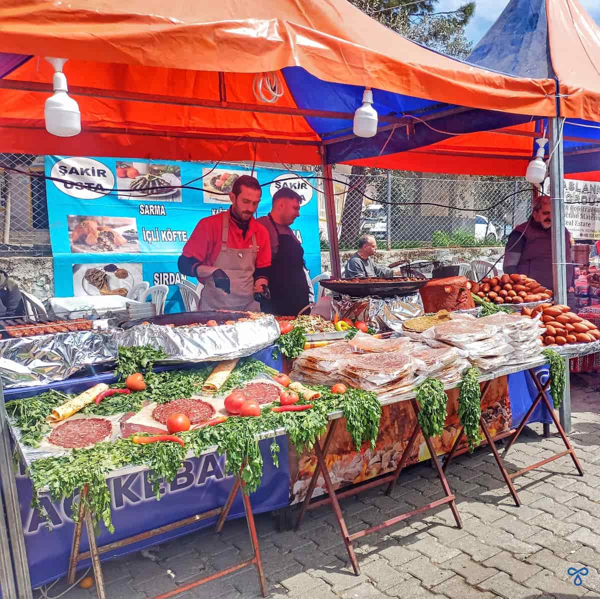 A street food stall with various meats for sale and an open pan for cooking.
