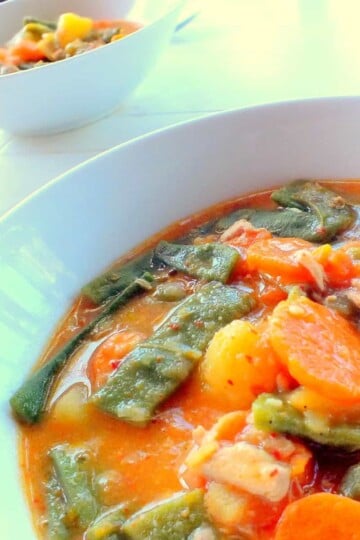 Two white bowls of soup. The soup is a thick consistency, orange in colour, and sliced carrots, green beans and potato is visible.