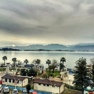 Looking out over the bay of Fethiye from above on a rainy day. The sky and sea are very grey and the park and car park are in the foreground.
