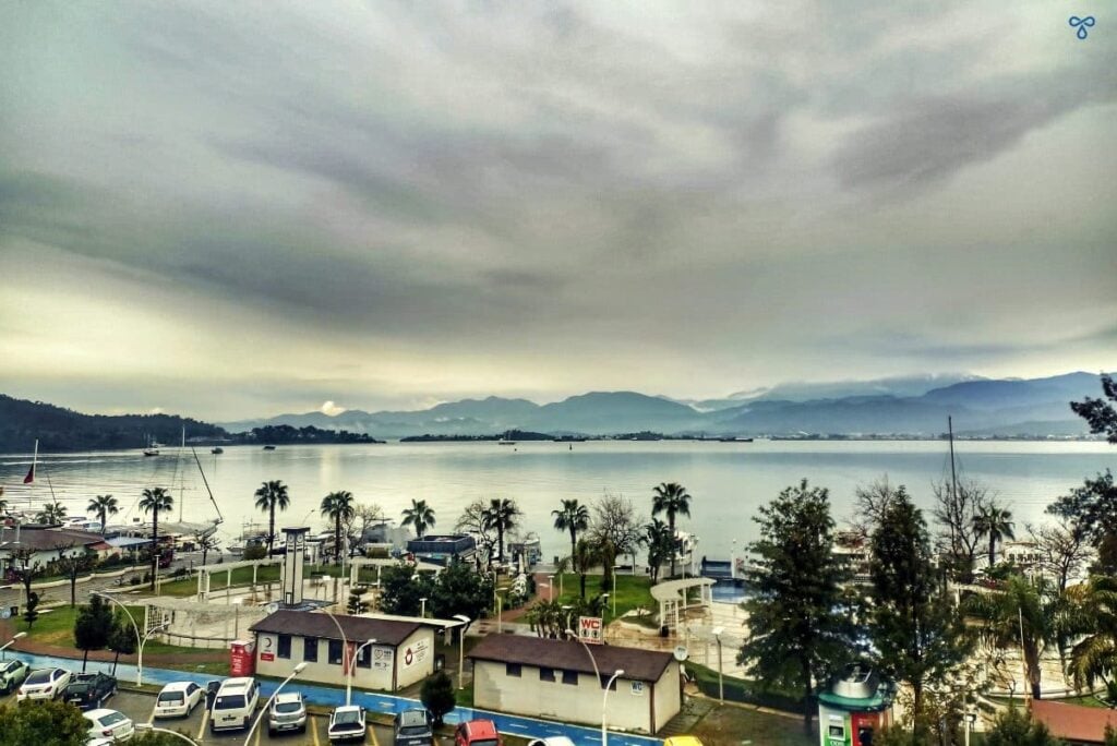 A view over the bay in Fethiye on a rainy day. Palm trees and a car park are in the foreground.