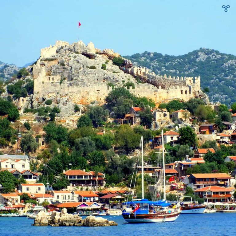 Rocky Simena overlooking the bay with citadel at the top. A gület is anchored in the bay.