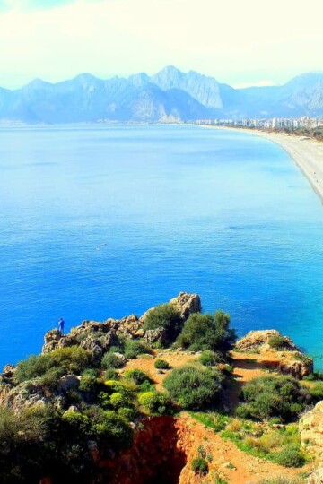 A high view along the stretch of Konyaaltı Beach with mountains in the background.