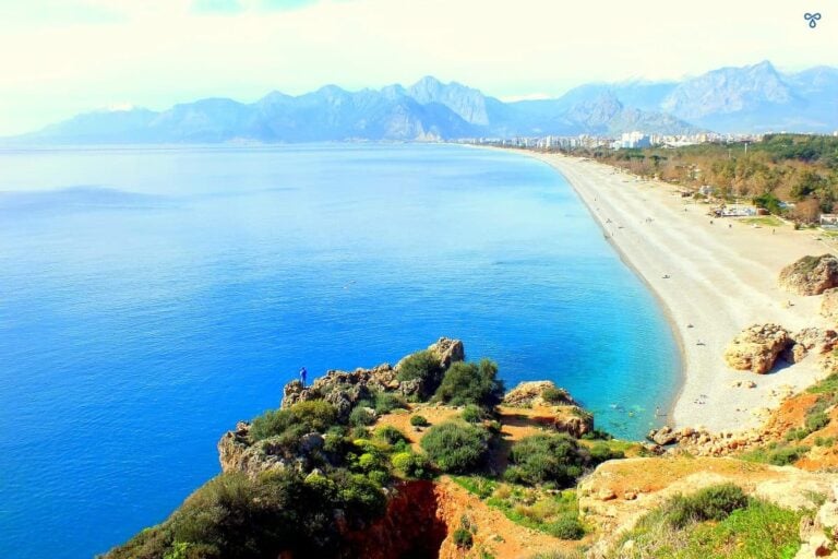 A high view along the stretch of Konyaaltı Beach with mountains in the background.