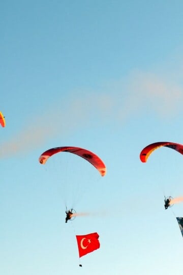 Three paramotors in the air. Atatürk flags and Turkish flags trail below them.