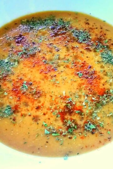 a bowl of soup viewed from above. The soup is orange coloured and topped with red chilli flakes and green dried mint.